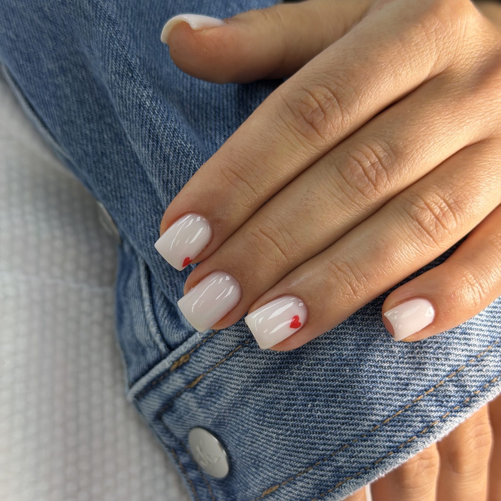 White manicure with tiny red heart accents at Hideaway Nail Design